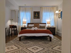 Room 16 at Stanton House Inn viewed through the doorway, with antique portrait above the queen bed, wool rug, and full-length mirror