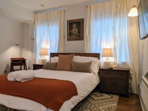 Queen bed with rust throw, velvet pillows, and antique portrait in Room 16 at Stanton House Inn, with writing desk visible at left