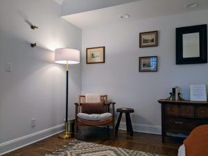 Reading corner with rattan chair, floor lamp, framed prints, and antique dresser in Room 16 at Stanton House Inn