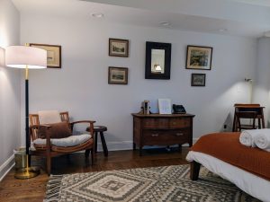 Rattan reading chair, floor lamp, antique dresser, and gallery of framed prints in Room 16 at Stanton House Inn, Greenwich CT
