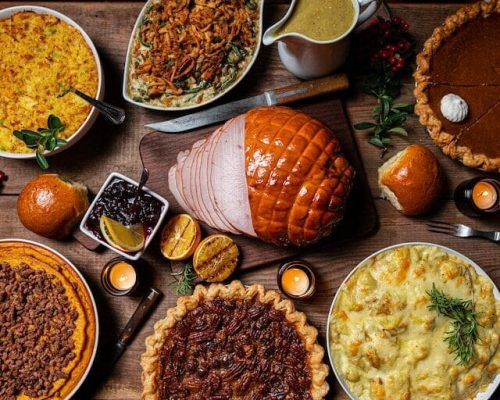 Pumpkin pie, a maple glazed ham, candied sweet potatoes, and a green bean casserole in the middle of a Thanksgiving table