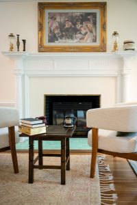 Books on a side table next to the comfortable modern seating beside the antique fireplace in the Brush Suite