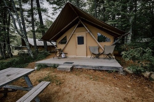 Glamping tent cabin with a queen bed, outdoor seating and picnic tables, and private bathrooms