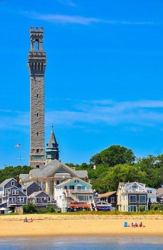 locals lounging on the sand of P-Town harbor in front of the Provincetown Town Hall and Pilgrim Monument
