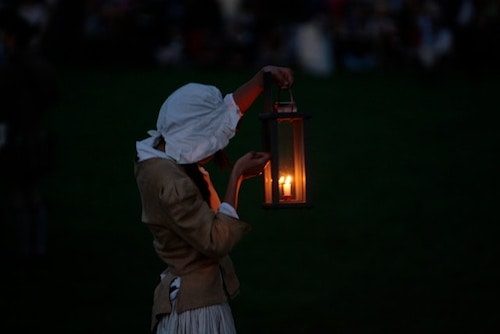 Woman reenactor lighting a lantern at dusk at one of the local historic sites, one of the best things to do in Lexington MA