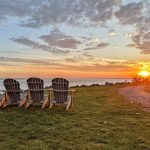 A line of Adirondack chairs facing the sunset and Island Beach at Greenwich Point Park