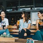 Three women chatting on a bench with drinks at a Greenwich outdoor bar