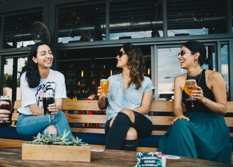 Three women chatting on a bench with drinks at a Greenwich outdoor bar