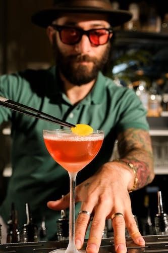 Bartending serving a unique cocktail to a human (no titles) at a gay bar that you can join while you're here