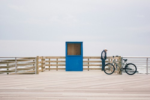 Man pondering the waves on the sandy shores from the boardwalk on Long Beach, Long Island