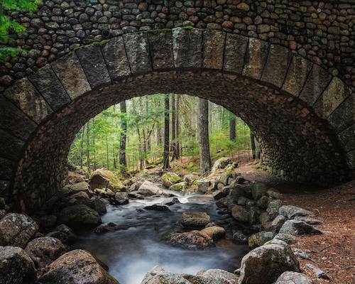 Stone arch bridge over a peaceful brook in a lush forest along the carriage roads of Acadia National Park
